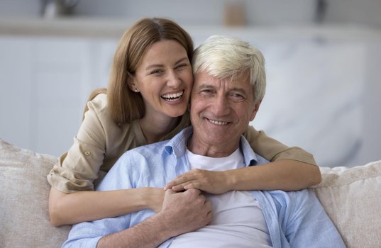 Woman hugging her smiling father on the sofa