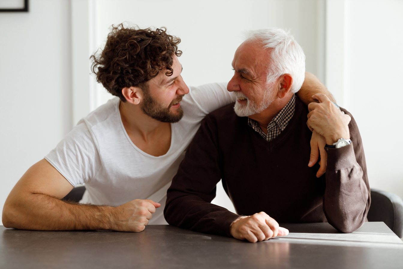 Young man with his arm around his father at the kitchen table
