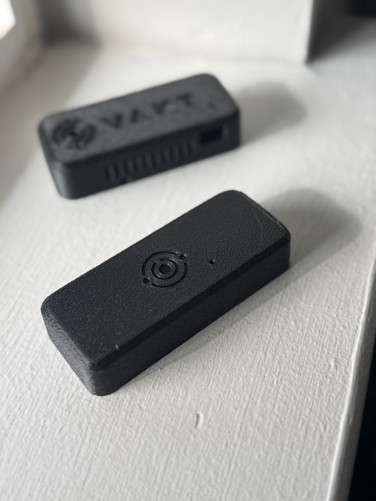 A VAKT node in front of a VAKT hub, both small black boxes on a white windowsill